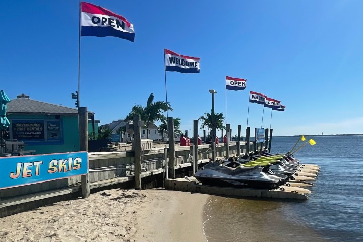 Beachside jet ski rental with open flags and lined up jet skis at a dock.