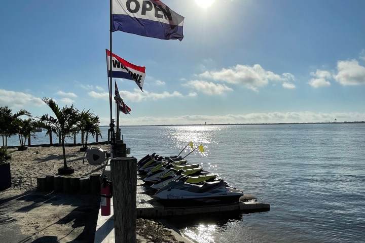Beach with jet skis, palm trees, and open sign at sunrise.