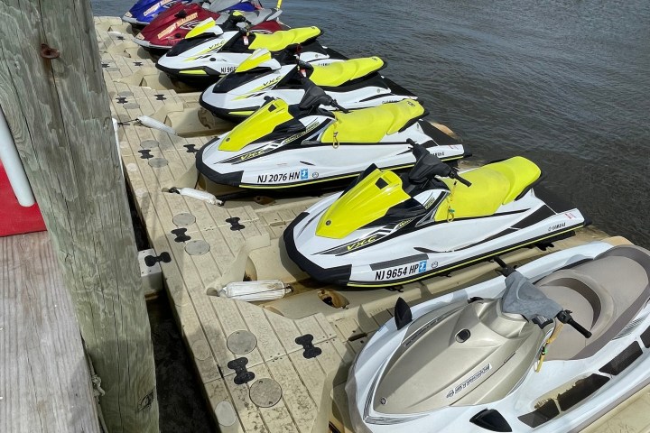Several jet skis docked on a floating platform by the water, all with bright yellow seats.